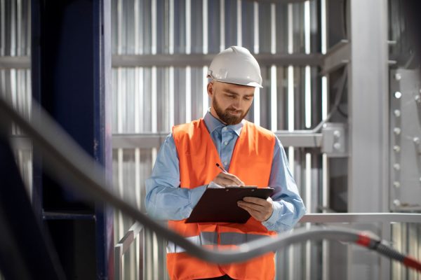 Electrician conducting an inspection and recording findings on a clipboard.